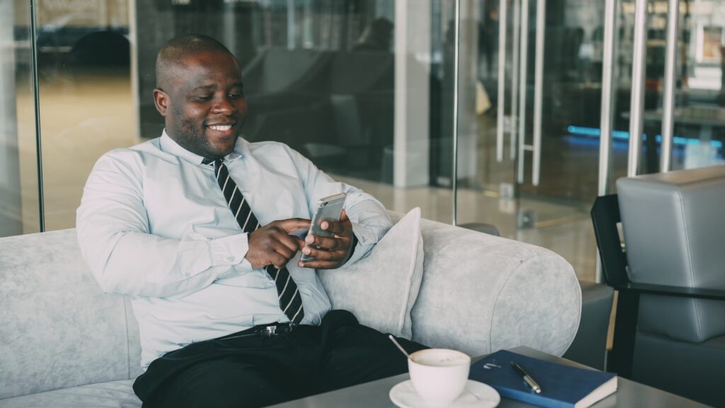Man in shirt and tie laughing while looking at phone.