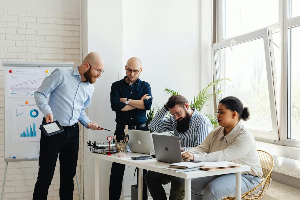 A diverse team discusses strategy in a modern office setting with laptops and charts.