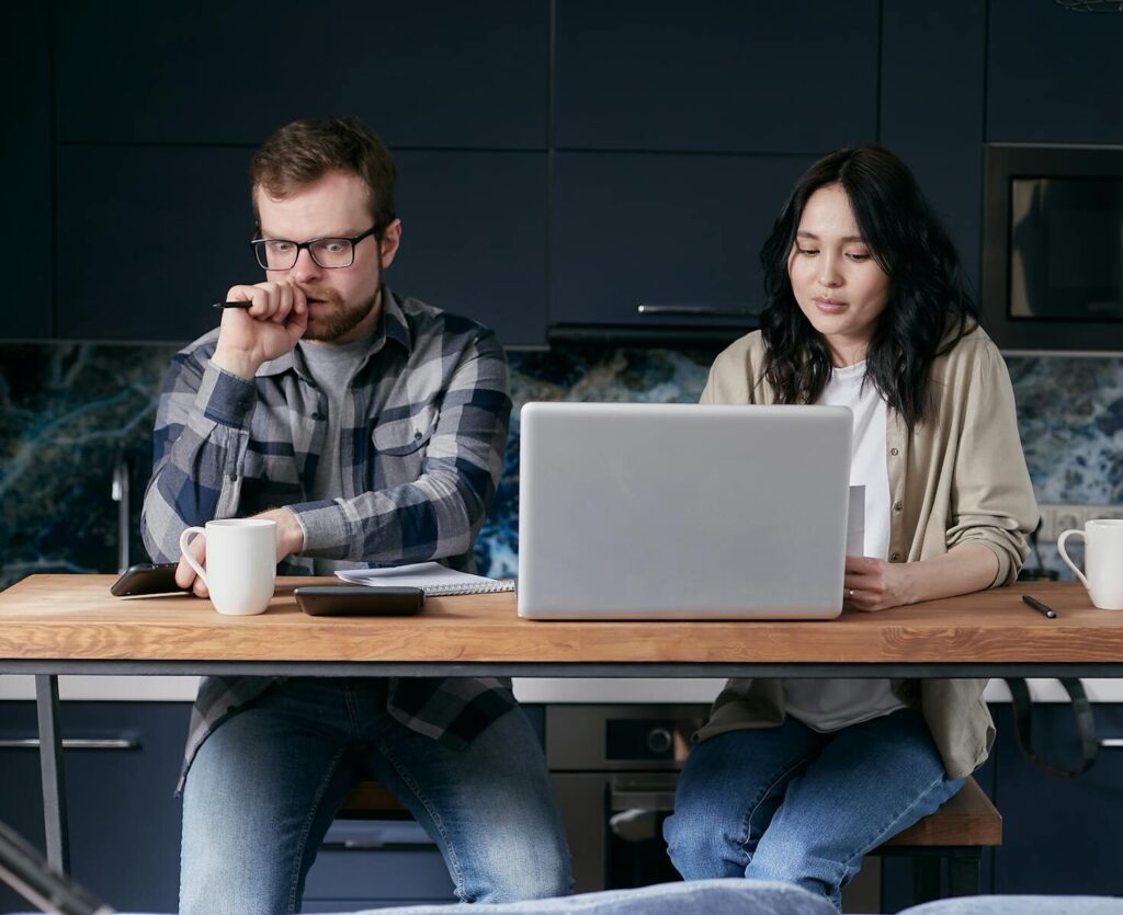 Couple working together in kitchen, focused on laptop tasks and discussions.
